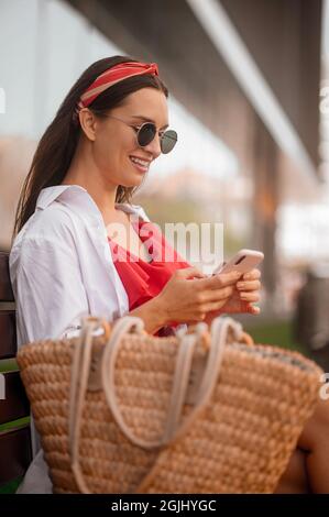 Eine niedliche junge Frau in Sonnenbrille mit einem Telefon in den Händen Stockfoto