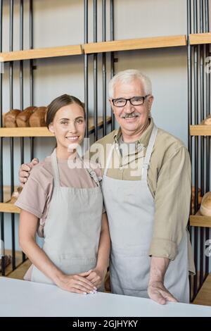 Porträt eines glücklichen älteren Mannes, der seine Tochter gegen die Ausstellung umarmt und in der Bäckerei zusammenarbeitet Stockfoto