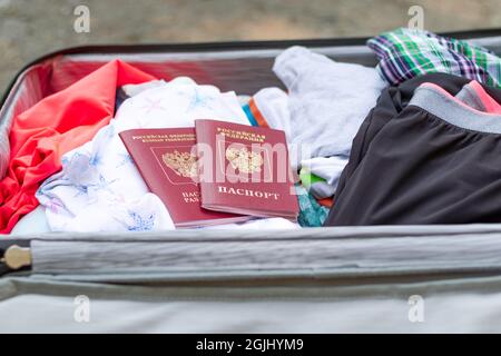 An einem sonnigen Sommertag liegt ein offener Koffer mit Dingen und zwei Pässen auf der Straße. Selektiver Fokus Stockfoto