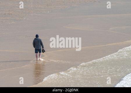 Ein Mann, der allein am Fistral Beach in Newquay in Cornwall entlang der Küste läuft. Stockfoto