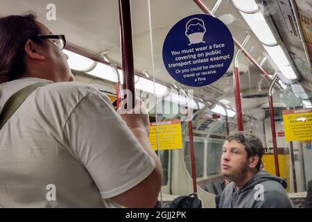 London, Großbritannien. 10. August 2021. Ein Paar, das keine Gesichtsbedeckung auf der U-Bahn-Linie der Bakerloo Line neben einem Schild trägt, auf dem steht, dass Gesichtsbedeckungen in öffentlichen Verkehrsmitteln erforderlich sind, sofern sie nicht von der Ausnahme ausgenommen sind. Während die Sommerferien zu Ende gehen, aber die Covid-19-Pandemie weiter anhält, werden die Arbeitnehmer ermutigt, in die Hauptstadt zurückzukehren, aber es besteht die Sorge, dass der fehlende weitverbreitete Einsatz von Gesichtsmasken in der U-Bahn, in Bussen und Zügen sie davon abhalten wird, massenhaft zurückzukehren. Kredit: Stephen Chung / Alamy Live Nachrichten Stockfoto