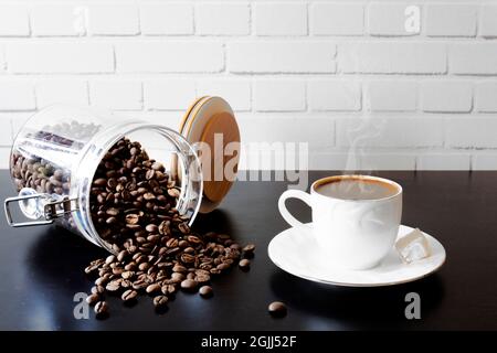 Vor einer weißen Backsteinmauer, auf schwarzem Hintergrund, eine Tasse türkischer Kaffee, türkischer Genuss, Kanne und ein Glas Bohnen. Selektiver Fokus. Stockfoto
