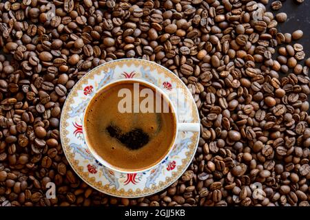 Kaffeebohnen im Hintergrund und eine Tasse schaumigen türkischen Kaffee darauf. Selektiver Fokus. Stockfoto