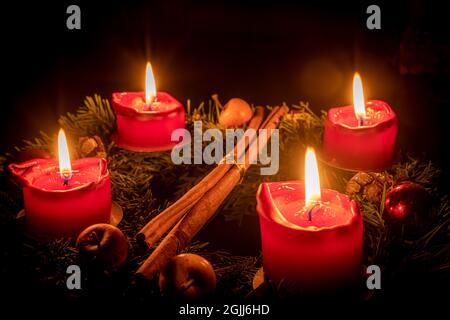 Dekorierter Adventskranz aus Tannenzweigen mit brennenden roten Kerzen vor schwarzem Hintergrund Stockfoto