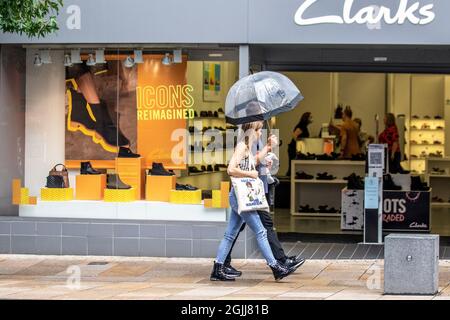 Symbole in Preston, Lancashire, neu vernagnt. Wetter in Großbritannien 10. September 2021. Clarkes Shoe Shops, Shopper, Frau beim Shoppen in gelbem Anorak an einem Showery-Tag im Preston City Centre. Kredit; MediaWorldImages/AlamyLiveNews Stockfoto