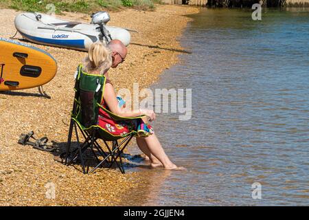 Paar sitzen auf Stühlen am Strand und paddeln ihre Füße im Meer an einem heißen Septembertag, England, Großbritannien Stockfoto