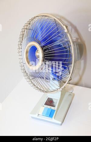 Vertikale Nahaufnahme eines kleinen elektrischen Ventilators auf einem weißen Tisch. Stockfoto