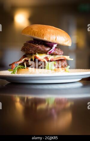 Köstlicher klassischer cheeburger, der in einem Restaurant auf einem weißen Teller auf einem Holztisch serviert wird Stockfoto