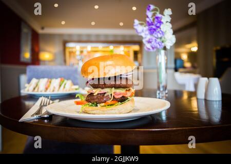 In einem Restaurant wird ein köstlicher klassischer Burger auf einem weißen Teller auf einem Holztisch serviert Stockfoto