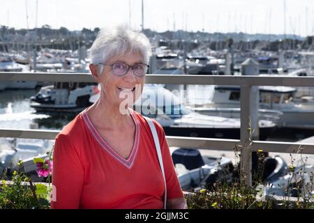 Eine ältere Frau, die vor einem Hafen sitzt Stockfoto