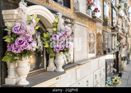 Gräber in Betonnischen mit Blumensträußen auf einem alten Friedhof. Stockfoto