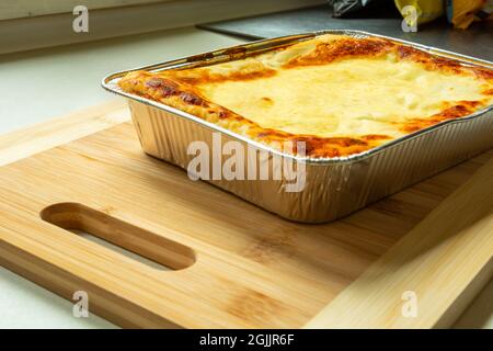 Köstliche gebackene Lasagne in einer Aluminiumschale auf einem Holzbrett Stockfoto