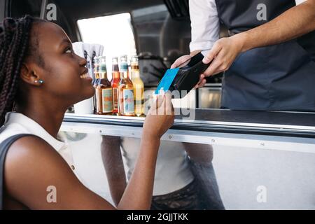 Nahaufnahme einer lächelnden Frau, die mit einer Kreditkarte bezahlt, während sie an einem Foodtruck steht Stockfoto