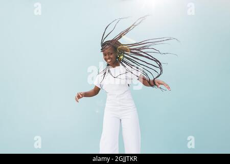 Glückliche Frau in Casuals, die ihr langes geflochtenes Haar in der Luft an der Wand fliegen lässt Stockfoto