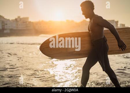 Männlicher Afro-Surfer, der während der Sonnenuntergangszeit Spaß beim Surfen hat - Afrikanischer Mann am Tag der Brandung - Extremsport Lifestyle Menschen Konzept Stockfoto