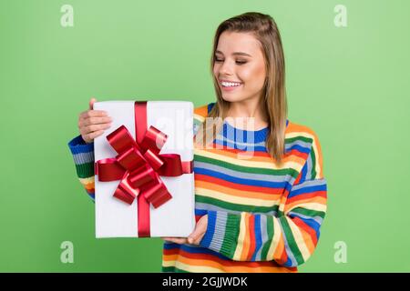 Foto Porträt Mädchen halten Geschenkbox lächelnd auf Geburtstagsfeier genießen in gestreiften Pullover isoliert pastellgrün Farbe Hintergrund Stockfoto