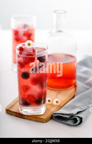 Zwei große Gläser mit vereisten roten Früchten, Saft und Flasche im Vordergrund Stockfoto