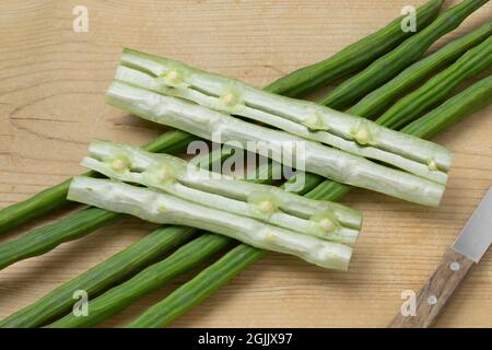 Frische rohe grüne ganze Moringa-Bohnen und Stecklinge mit Samen auf einem hölzernen Schneidebrett Stockfoto