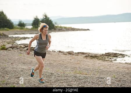 Die junge Sportlerin läuft morgens am Seeufer entlang Stockfoto