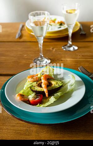 Bio-Salat mit Garnelen, Avocado, Tomaten, Olivenöl und Kräutern und Gläsern Weißwein auf einem Holztisch Stockfoto