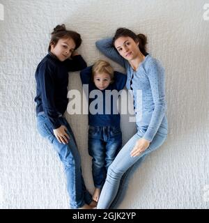 Mutter und zwei Kinder liegen im Bett, machen Herz, schauen in die Kamera und lächeln Stockfoto