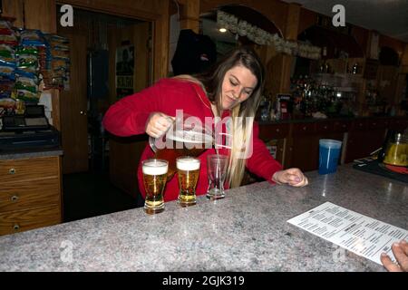 Eine Barkeeperin gießt Bier aus einem Krug in Gläser. Pierz Minnesota, USA Stockfoto