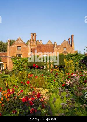 Viele farbenfrohe Dahlien im versunkenen Garten des Chenies Manor House, Buckinghamshire.eine Fülle von roten, orangefarbenen, violetten Dahlien in voller Blüte. Stockfoto
