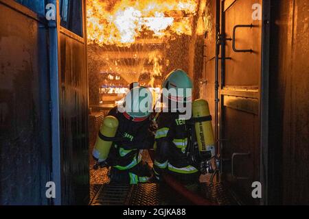 Pirna, Deutschland. September 2021. Zwei Feuerwehrleute bereiten sich im Behälter auf einen Überschlag vor, der gelöscht werden muss. Feuerwehren aus dem Landkreis Sächsische Schweiz-Osterzgebirge zu Szenarien im Feuertrainingscontainer. Quelle: Daniel Schäfer/dpa-Zentralbild/Daniel Schäfer/dpa/Alamy Live News Stockfoto