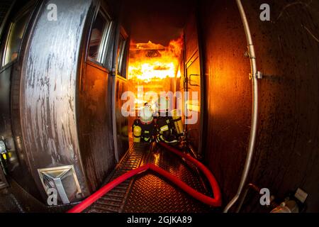 Pirna, Deutschland. September 2021. Zwei Feuerwehrleute bereiten sich im Behälter auf einen Überschlag vor, der gelöscht werden muss. Feuerwehren aus dem Landkreis Sächsische Schweiz-Osterzgebirge zu Szenarien im Feuerwehrtrainingsbehälter. Fisheye shot Quelle: Daniel Schäfer/dpa-Zentralbild/Daniel Schäfer/dpa/Alamy Live News Stockfoto