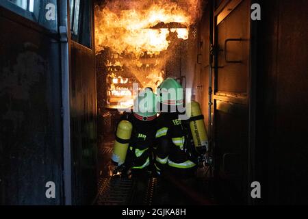 Pirna, Deutschland. September 2021. Zwei Feuerwehrleute bereiten sich im Behälter auf einen Überschlag vor, der gelöscht werden muss. Feuerwehren aus dem Landkreis Sächsische Schweiz-Osterzgebirge zu Szenarien im Feuertrainingscontainer. Quelle: Daniel Schäfer/dpa-Zentralbild/Daniel Schäfer/dpa/Alamy Live News Stockfoto