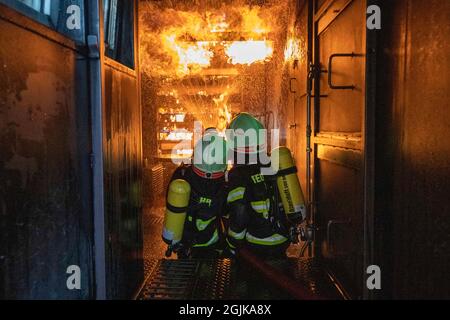 Pirna, Deutschland. September 2021. Zwei Feuerwehrleute bereiten sich im Behälter auf einen Überschlag vor, der gelöscht werden muss. Feuerwehren aus dem Landkreis Sächsische Schweiz-Osterzgebirge zu Szenarien im Feuertrainingscontainer. Quelle: Daniel Schäfer/dpa-Zentralbild/Daniel Schäfer/dpa/Alamy Live News Stockfoto