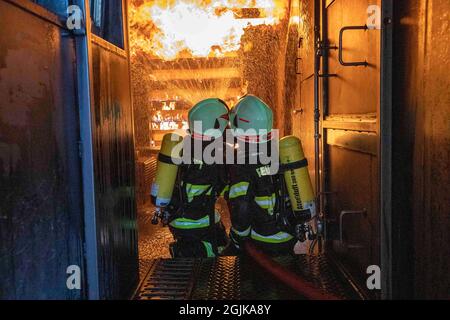 Pirna, Deutschland. September 2021. Zwei Feuerwehrleute bereiten sich im Behälter auf einen Überschlag vor, der gelöscht werden muss. Feuerwehren aus dem Landkreis Sächsische Schweiz-Osterzgebirge zu Szenarien im Feuertrainingscontainer. Quelle: Daniel Schäfer/dpa-Zentralbild/Daniel Schäfer/dpa/Alamy Live News Stockfoto