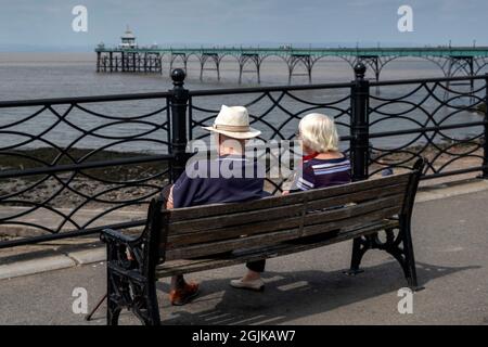 Ein älteres Paar, das auf einer Bank mit Blick auf den Clevedon Pier sitzt Stockfoto