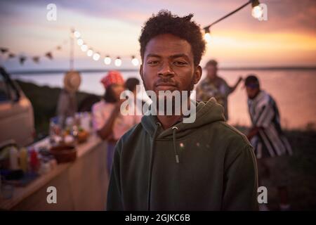 Porträt eines jungen afrikanischen Mannes, der die Kamera anschaut, während er sich auf einer Strandparty amüsieren kann Stockfoto