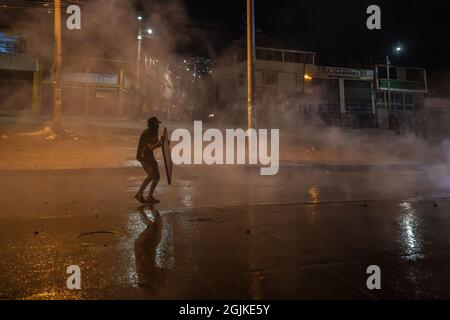 Bogota, Kolumbien. September 2021. Ein Protestler hält einen Schild hoch, während Polizeibeamte während der Demonstration Wasserkanonen sprühen. Der Streik ist eine Reaktion auf den Jahrestag, an dem die Polizei vor einem Jahr in Bogota, Kolumbien, in einer Nacht 13 Menschen getötet hat. Der Protest ist Teil eines laufenden nationalen Streiks, der am 28. April in Kolumbien als Reaktion auf Steuerreformen begann, die die Ärmsten des Landes zum Ziel hätten. Kredit: SOPA Images Limited/Alamy Live Nachrichten Stockfoto