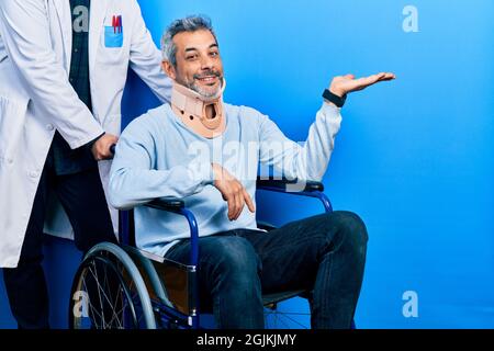 Schöner Mann mittleren Alters mit grauen Haaren auf dem Rollstuhl trägt Halsband lächelnd fröhlich präsentiert und zeigt mit Handfläche Blick auf die Stockfoto