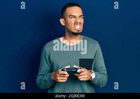 Junger afroamerikanischer Mann spielt Videospiel, der Controller wütend und wütend schreit, frustriert und wütend, schreiend vor Wut. Wut und Agress Stockfoto