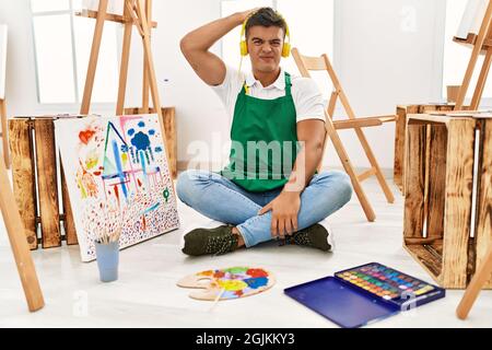 Junger hispanischer Mann im Kunststudio verwirrt und wundert sich über Fragen. Unsicher mit Zweifel, Denken mit Hand auf Kopf. Nachdenkliches Konzept. Stockfoto