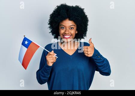 Junge afroamerikanische Frau, die die chilenische Flagge hält, lächelt glücklich und positiv, tut mit dem Daumen hoch und tut ein ausgezeichnetes und positives Zeichen Stockfoto