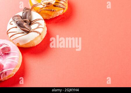 Foto von einem weißen Schokoladendonut und zwei halbfarbigen Donuts auf rotem Hintergrund.das Foto hat Kopierraum und ist im horizontalen Format aufgenommen. Stockfoto