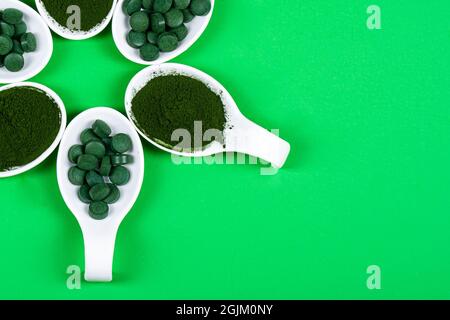 Chlorella oder Spirulina in Form von Tabletten und Pulver auf grünem Hintergrund, Nahaufnahme. Stockfoto