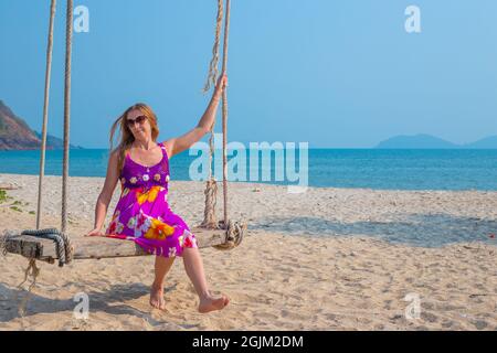 Junge Frau schwingt auf einer Schaukel, die an einer Palme am Meer hängt. Reisen und Tourismus in die tropischen Länder Asiens. Stockfoto