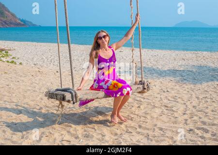 Junge Frau schwingt auf einer Schaukel, die an einer Palme am Meer hängt. Reisen und Tourismus in die tropischen Länder Asiens. Stockfoto