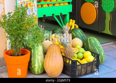 Ein Korb mit verschiedenen frischen Öko-Sommerfrüchten steht auf einer Straße vor einem Lebensmittelgeschäft, Supermarkt. Wassermelonen, Äpfel, Bananen, Zitrusfrüchte, Ananas Stockfoto
