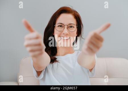 Lächelnde junge Frau aus der Nähe mit Brille zeigt den Daumen nach oben. Stockfoto