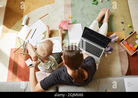 Direkt über dem Bild der Multitasking-Mutter, die auf dem Boden sitzt, während sie gleichzeitig mit dem Sohn arbeitet und zeichnet Stockfoto