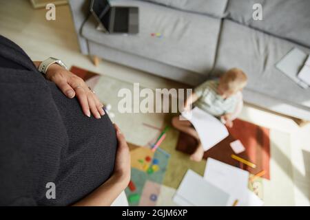 Oberhalb der unerkennbaren Schwangeren streichelte sie den Bauch, während ihr Sohn auf dem Teppich saß und zeichnete Stockfoto