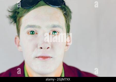 Kerl mit weißem Make-up im Gesicht und grünen Haaren. Schmiernase von Clown oder Pantomime. Mann Schauspieler im Anzug schaut auf die Kamera. Theaterkonzept. Stockfoto