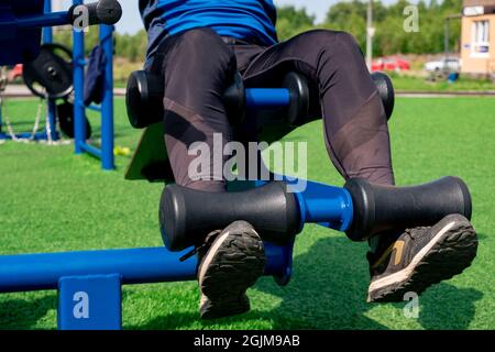 Beine einer Person, Durchführung von Bauchübungen mit einem Outdoor-Trainingsgerät Sit-up-Bank Stockfoto