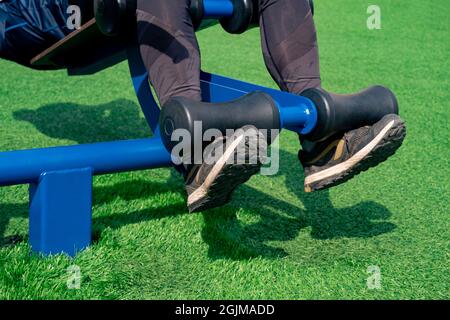 Beine einer Person, Durchführung von Bauchübungen mit einem Outdoor-Trainingsgerät Sit-up-Bank Stockfoto